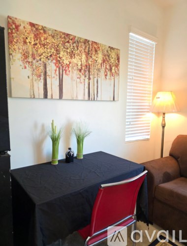 A table with a black cloth and a red chair in front of a painting of trees.
