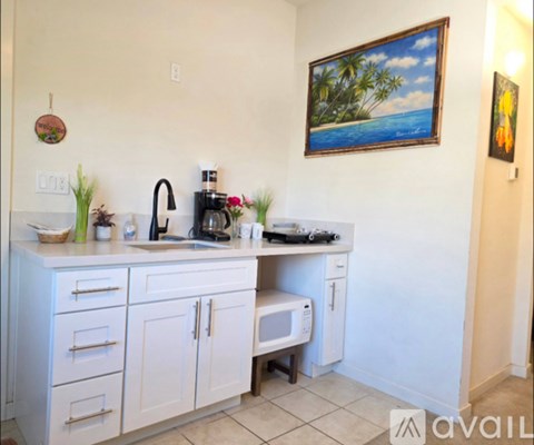 A kitchen with white cabinets and a painting of a beach scene on the wall.