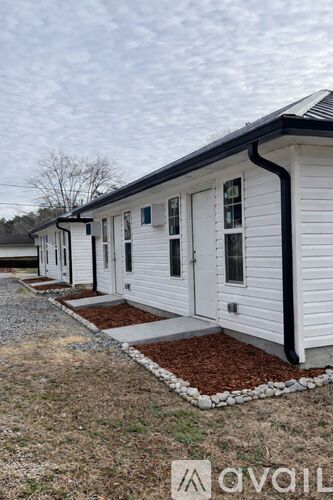 A row of white mobile homes with black trim and brown mulch in front.