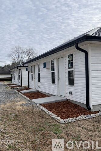 A row of white mobile homes with black trim and brown mulch in front.
