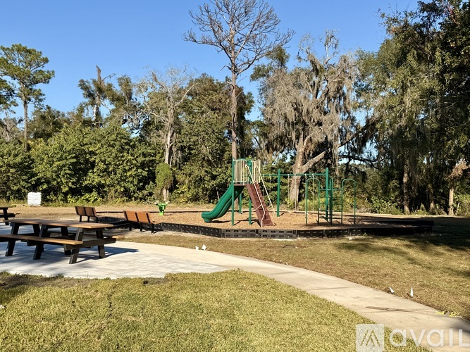 A playground with a green slide and picnic tables surrounded by trees.