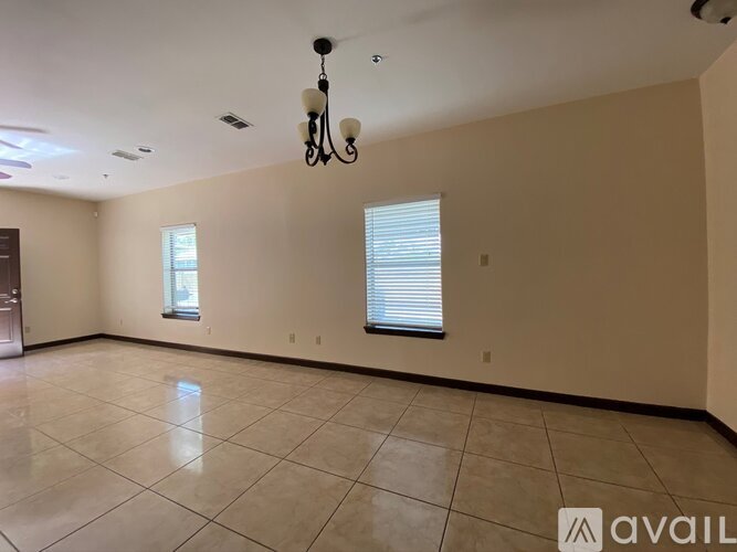 A spacious room with a chandelier, tiled floor, and two windows.