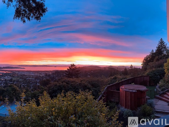 A sunset view from a hilltop with a pool and buildings in the distance.