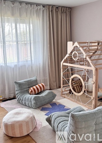 A living room with a striped ottoman and a wooden house-shaped structure.