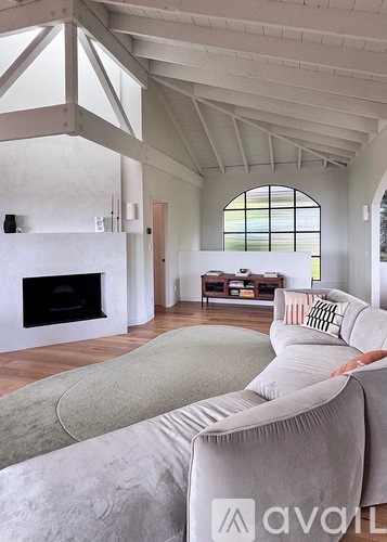 A person is sitting on a grey couch in a spacious room with a fireplace and a large window.