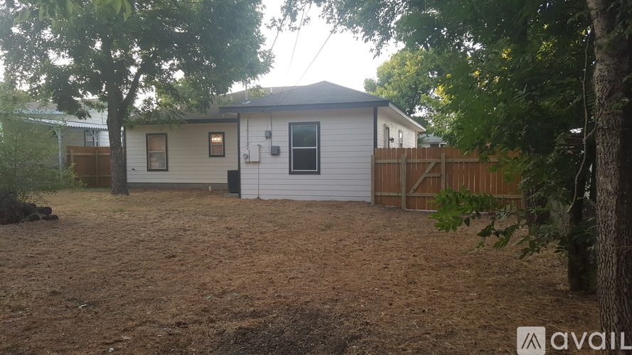A house with a brown roof and a white exterior is surrounded by trees and has a dirt ground.