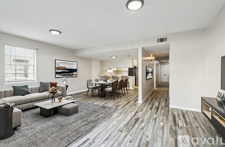 A spacious living room with a grey sofa, a coffee table, and a dining table with chairs.