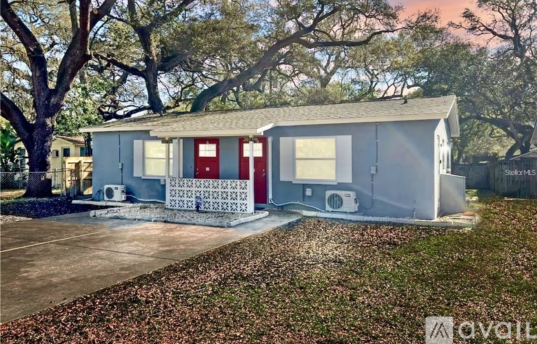 A small white house with a red door and windows is surrounded by trees.