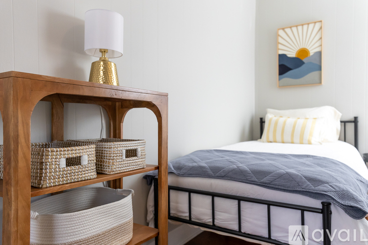 A bedroom with a bed, a nightstand with a lamp, and a painting on the wall.
