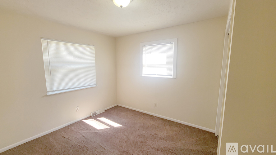 A room with a carpeted floor, a window with blinds, and a ceiling light.