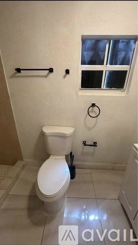 A white toilet in a bathroom with a window above it.