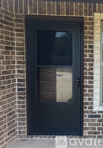 A black door with a glass window is set in a brick wall.