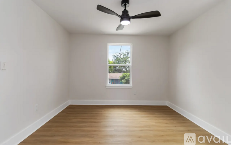 A room with a ceiling fan and a window showing a view of a tree and a building outside.
