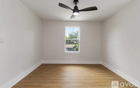 A room with a ceiling fan and a window showing a view of a tree and a building outside.