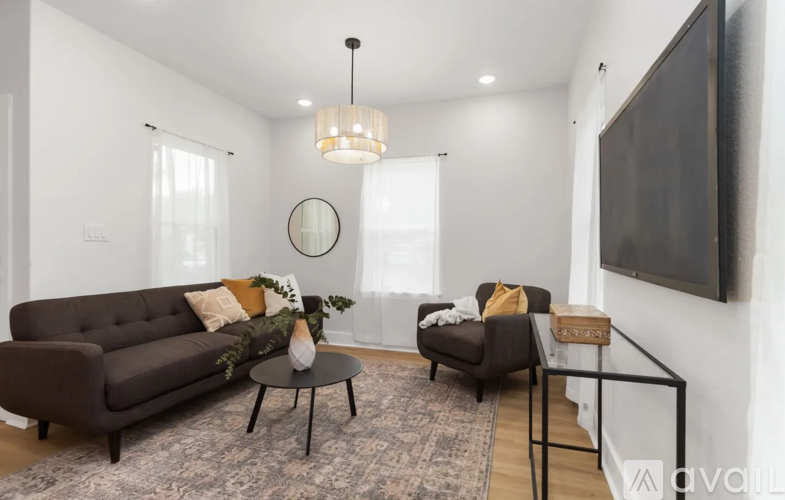 A living room with a brown sofa, a small table, and a TV mounted on the wall.