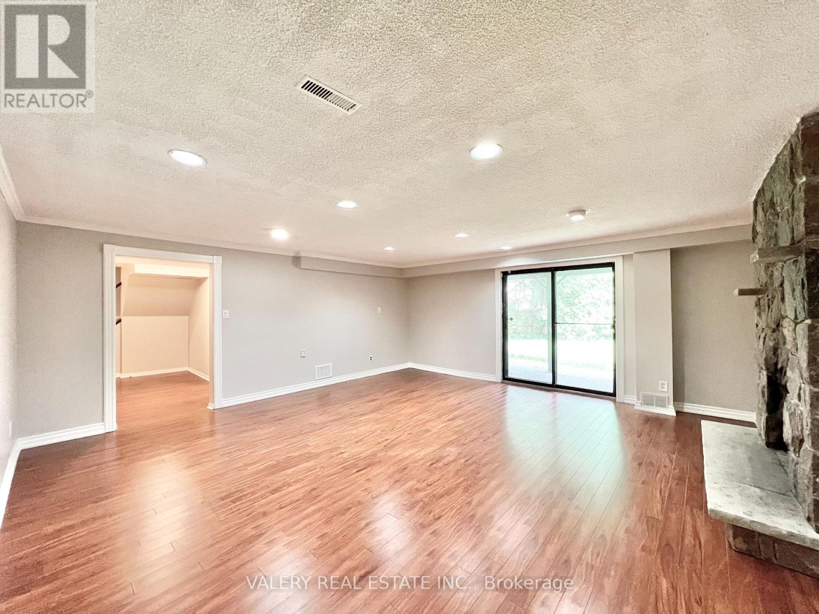 A spacious room with wood flooring and a stone fireplace.