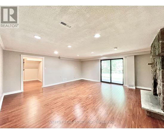 A spacious room with wood flooring and a stone fireplace.