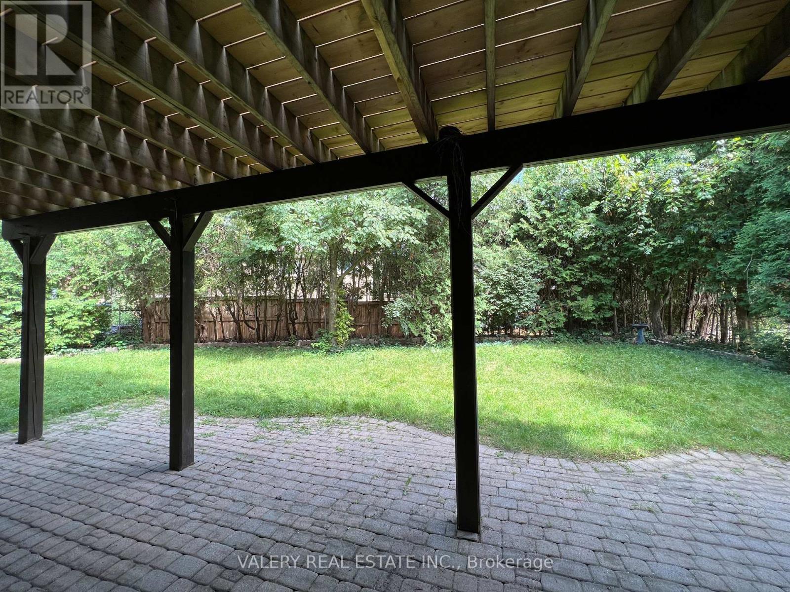 A patio with a roof and pillars is surrounded by a grassy area.