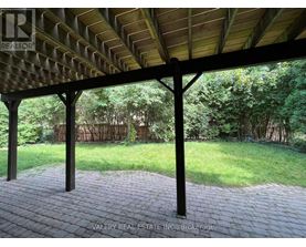 A patio with a roof and pillars is surrounded by a grassy area.