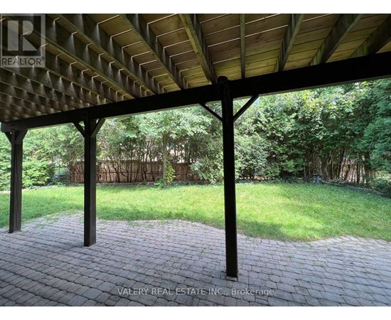 A patio with a roof and pillars is surrounded by a grassy area.