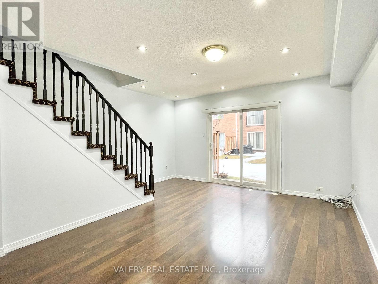 A spacious room with wooden floors and a staircase with black railings.