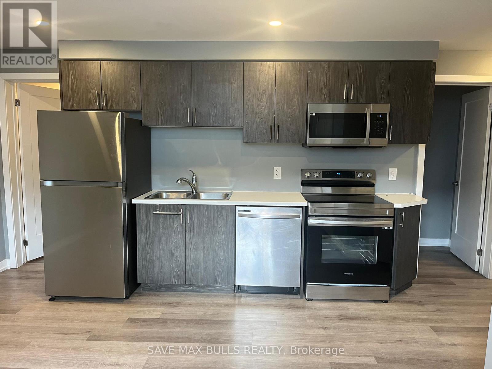 A kitchen with a refrigerator, sink, oven and microwave.