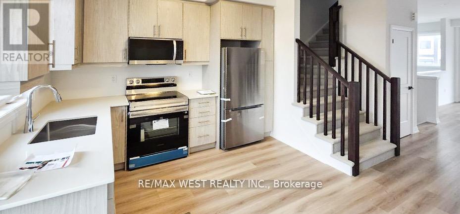 A kitchen with a refrigerator, microwave, oven and sink.