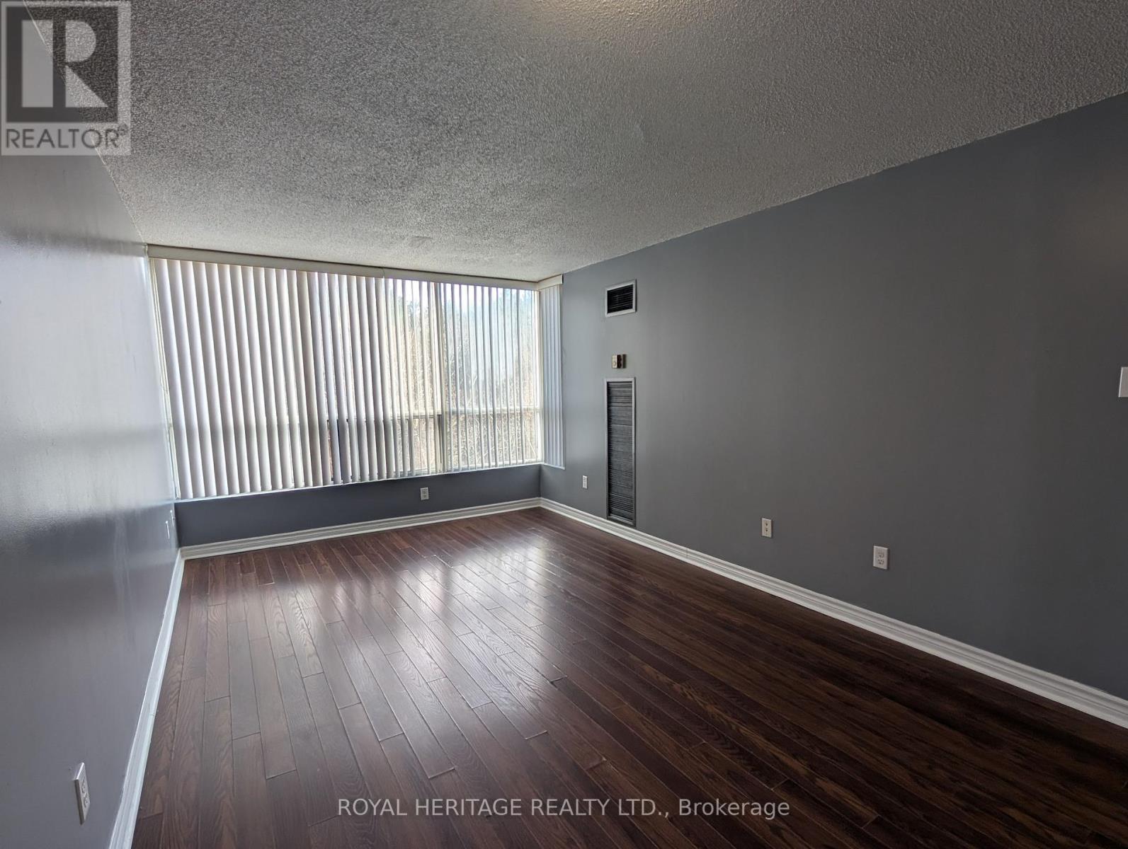 A spacious room with wooden floors and a large window with blinds.