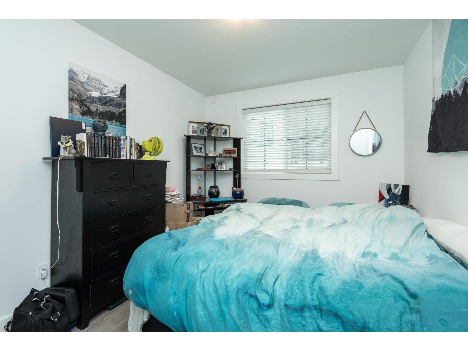 A bedroom with a blue bedspread and a black dresser.