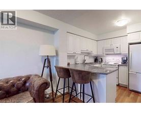 A brown leather sofa sits in a kitchen with white cabinets and a granite countertop.