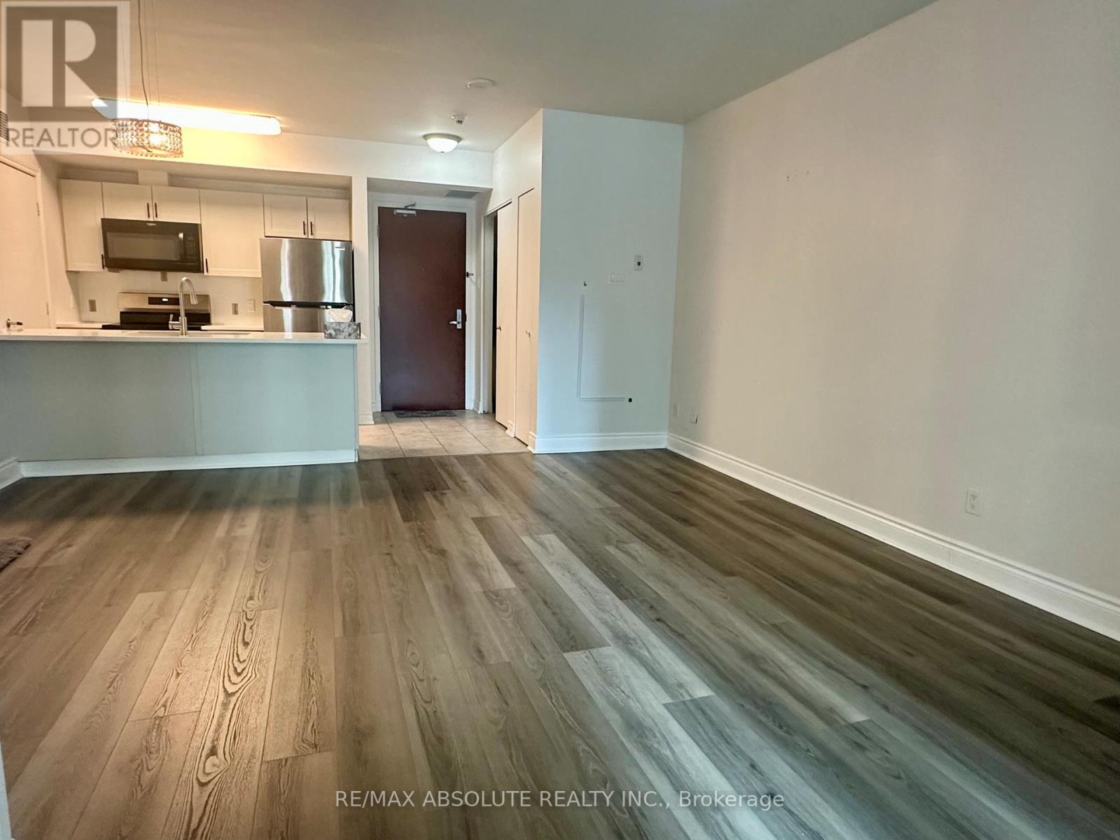 A room with a wooden floor and a kitchenette in the background.