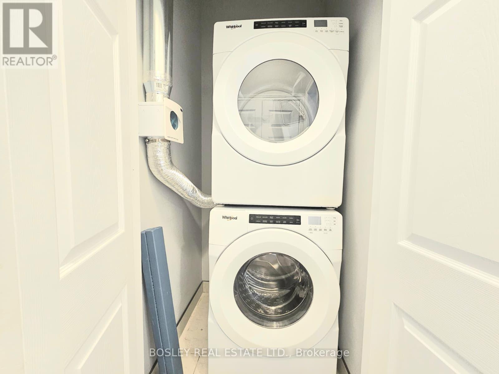 A white dryer is stacked on top of another white dryer in a small space.