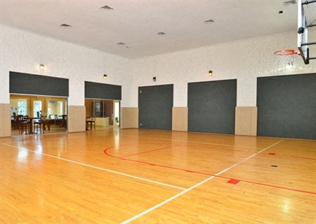 A basketball court inside a gym with a basketball hoop on the right side.