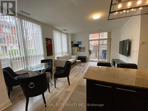 A well-lit living room with a glass table and black chairs.