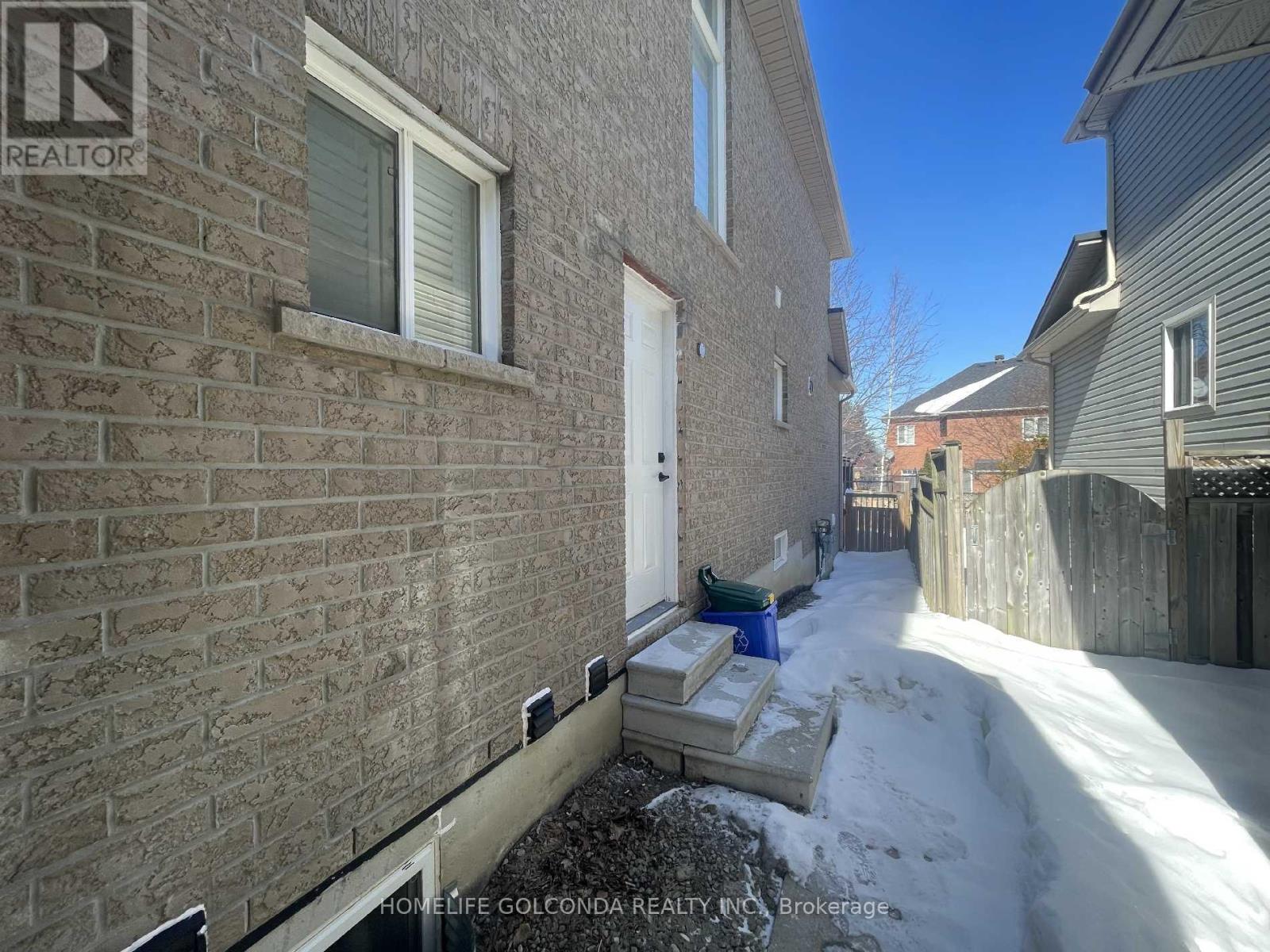 A snowy alley with a brick building on the left and a wooden fence on the right.