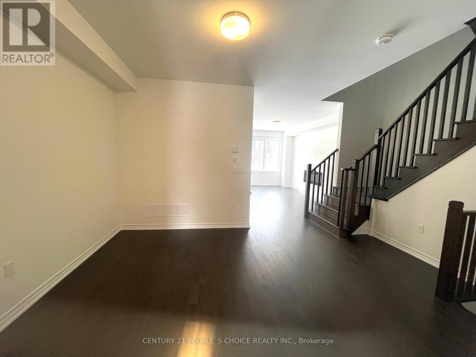 A spacious room with wooden floors and a staircase with black railings.