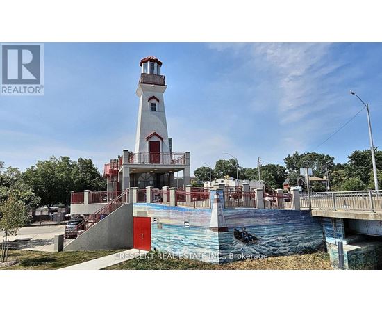 A lighthouse is in front of a pool and a bridge.
