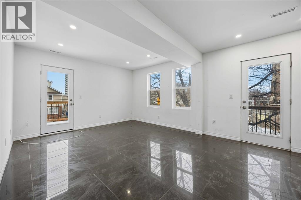 A spacious room with a marble floor and white walls, with windows showing a view of a tree and a building.
