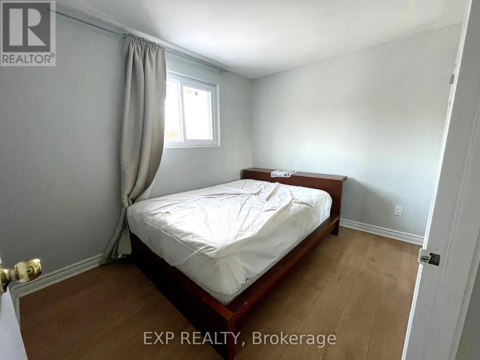 A bedroom with a bed, wooden floors, and a window with curtains.