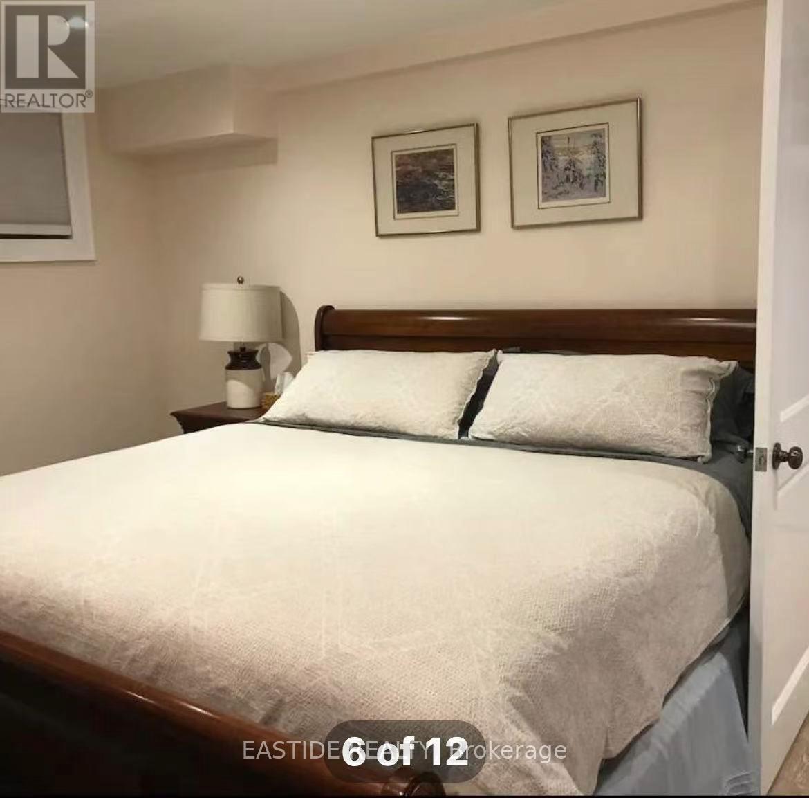 A bedroom with a bed, nightstand, lamp, and two pictures on the wall.