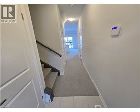A hallway with a staircase and a wall-mounted device on the wall.