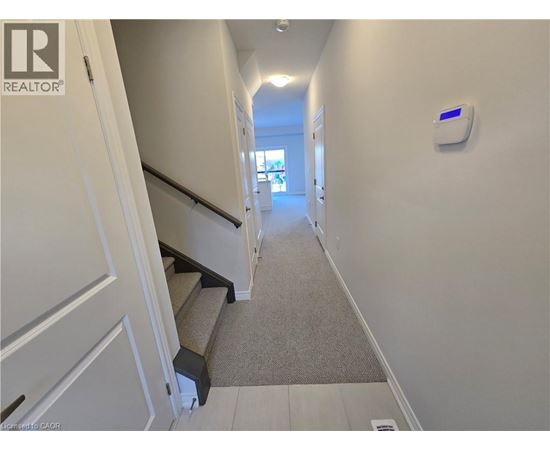 A hallway with a staircase and a wall-mounted device on the wall.