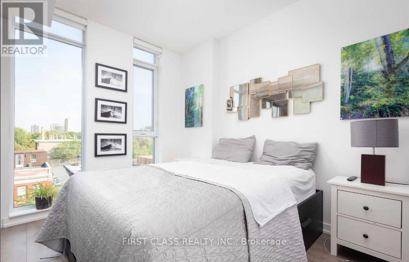 A bedroom with a large bed, a nightstand with a lamp, and pictures on the wall.