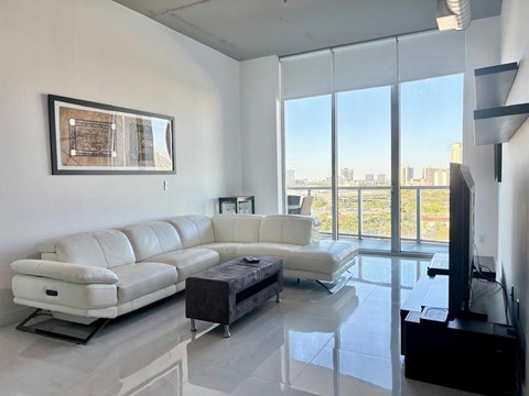 A living room with a white leather couch and a black ottoman.