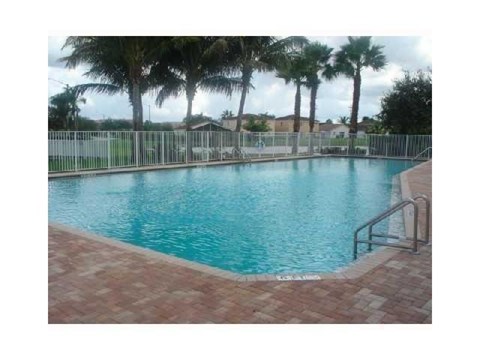 A pool surrounded by palm trees and a metal fence.