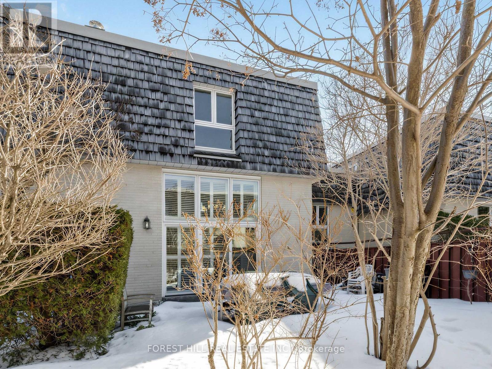 A house with a black roof and a white window is surrounded by bare trees and snow.
