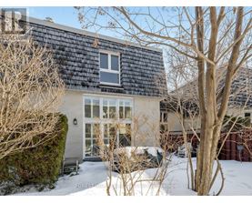 A house with a black roof and a white window is surrounded by bare trees and snow.