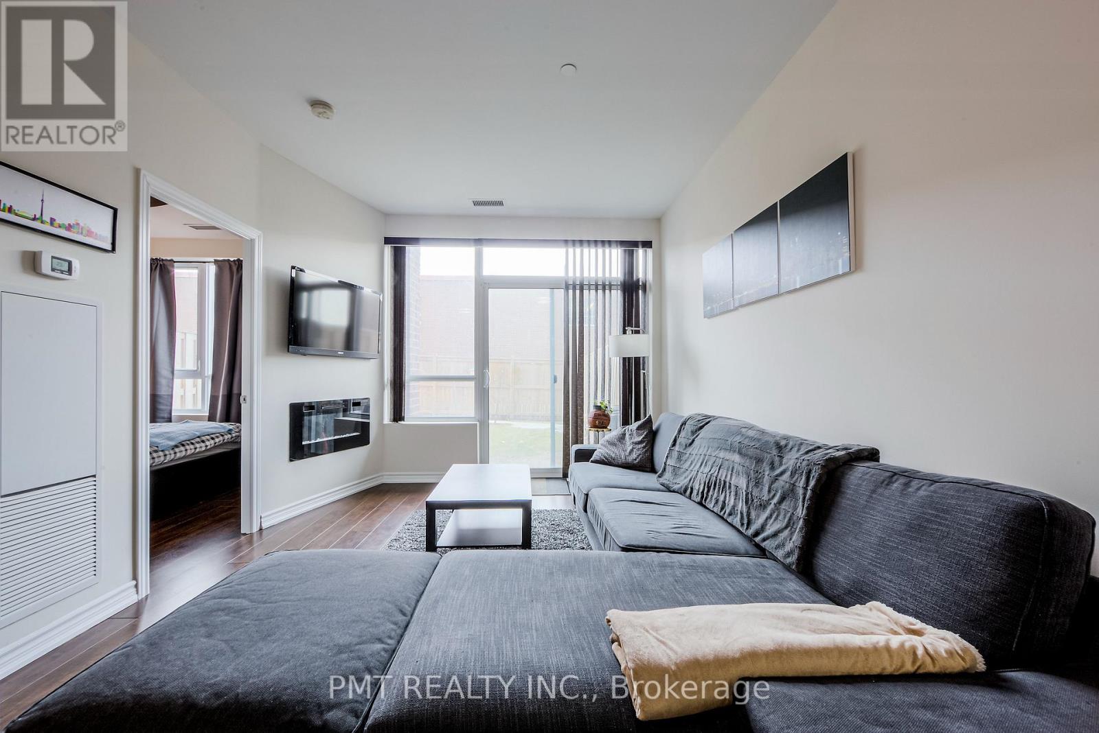 A living room with a black couch and a flat screen TV mounted on the wall.