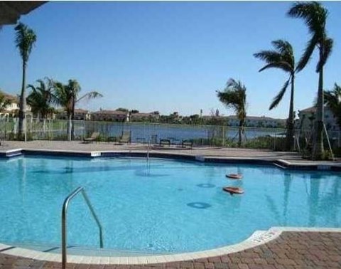 A pool with a metal ladder and palm trees in the background.