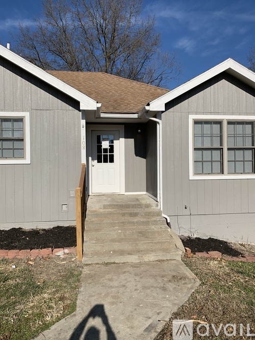 A grey house with a brown roof and a white door.